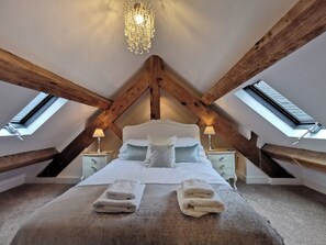 A bedroom with a sloped ceiling, wooden beams, a bed with pillows, two bedside tables with lamps, and a skylight. - 7 bedroom accommodation in Bradbourne, near Ashbourne (Bradbourne, near Ashbourne)