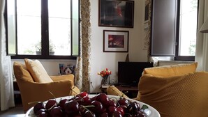 Een woonkamer met een groot raam, een televisie en een schaal kersen op een tafel.