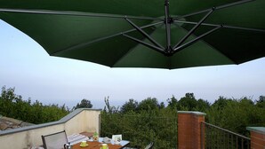 Een terras met een tafel gedekt voor twee personen, een groene parasol en uitzicht op de omliggende begroeiing.