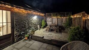 A patio area with stone walls, outdoor furniture, and string lights. - Spacious, luxury,  romantic Barn for couples near Exmoor & Coast  (Bratton Fleming, Barnstaple)