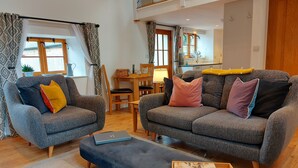 A modern living room with two grey sofas, a coffee table, and a dining area with a wooden table and chairs. - Spacious, luxury,  romantic Barn for couples near Exmoor & Coast  (Bratton Fleming, Barnstaple)