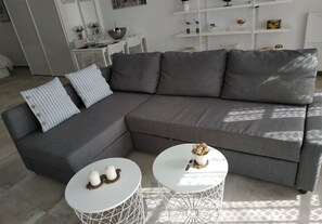 A modern living room with a grey sectional sofa, two white round tables, and a white coffee table with decorative items.