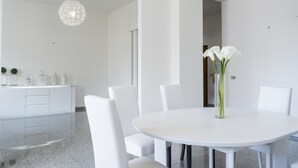 Un'elegante zona pranzo moderna con un tavolo bianco rotondo, sedie bianche e un vaso con fiori bianchi.