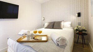 A neatly made bed with pillows, a tray with breakfast items, a bedside table with a plant, and a wall-mounted TV. - Picasso Boutique (Torremolinos)