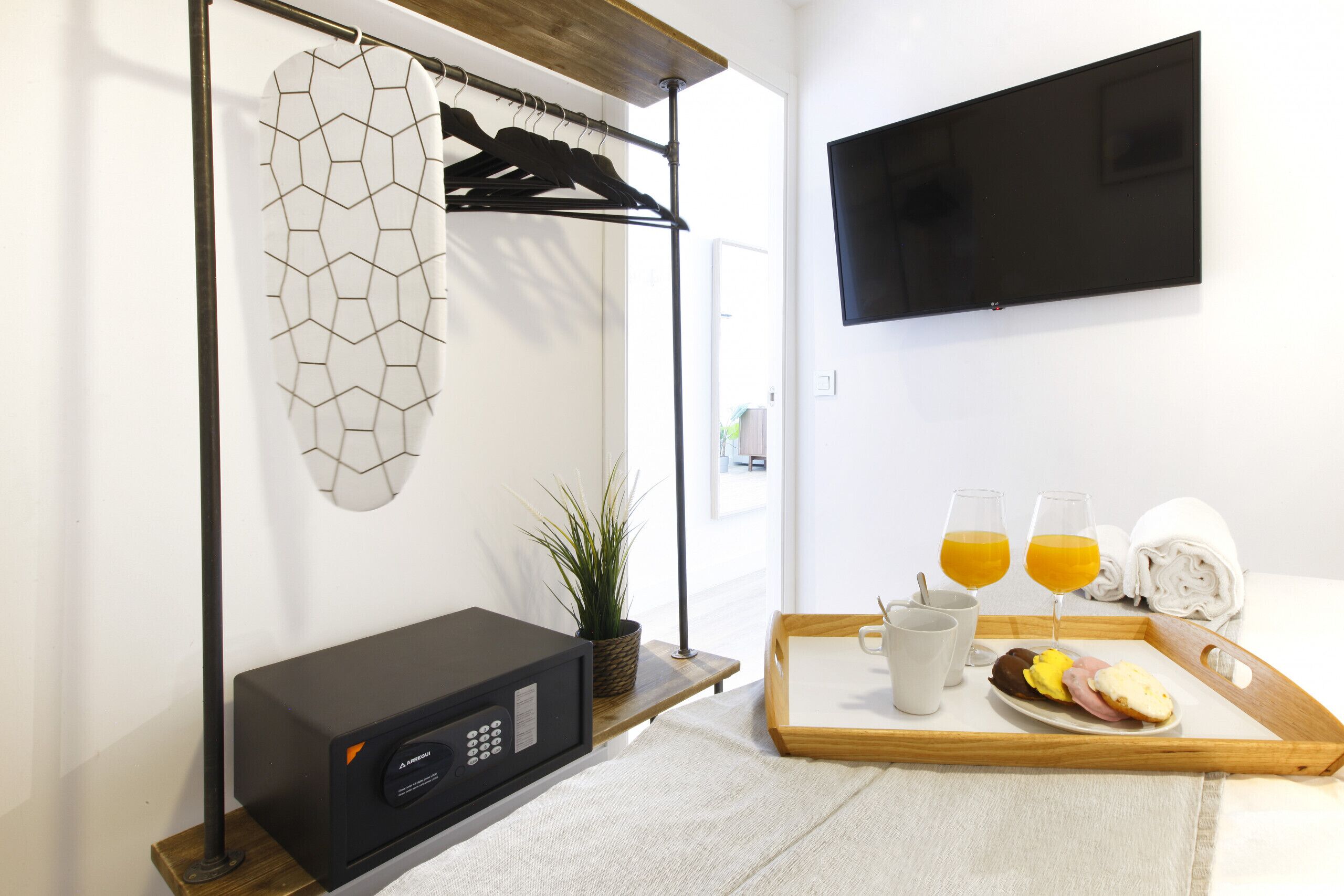 A hotel room with a bed, a TV mounted on the wall, a tray with breakfast items, a microwave, and a hanging coat rack.