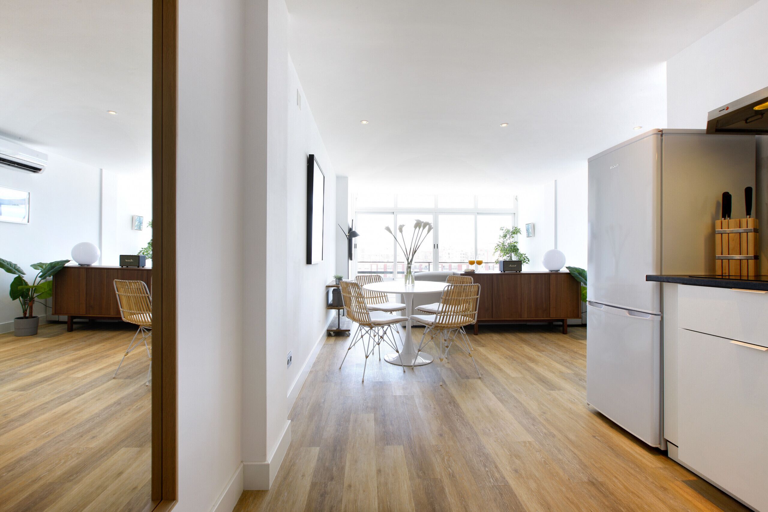 A modern kitchen with a dining area, wooden flooring, and a large window providing natural light.