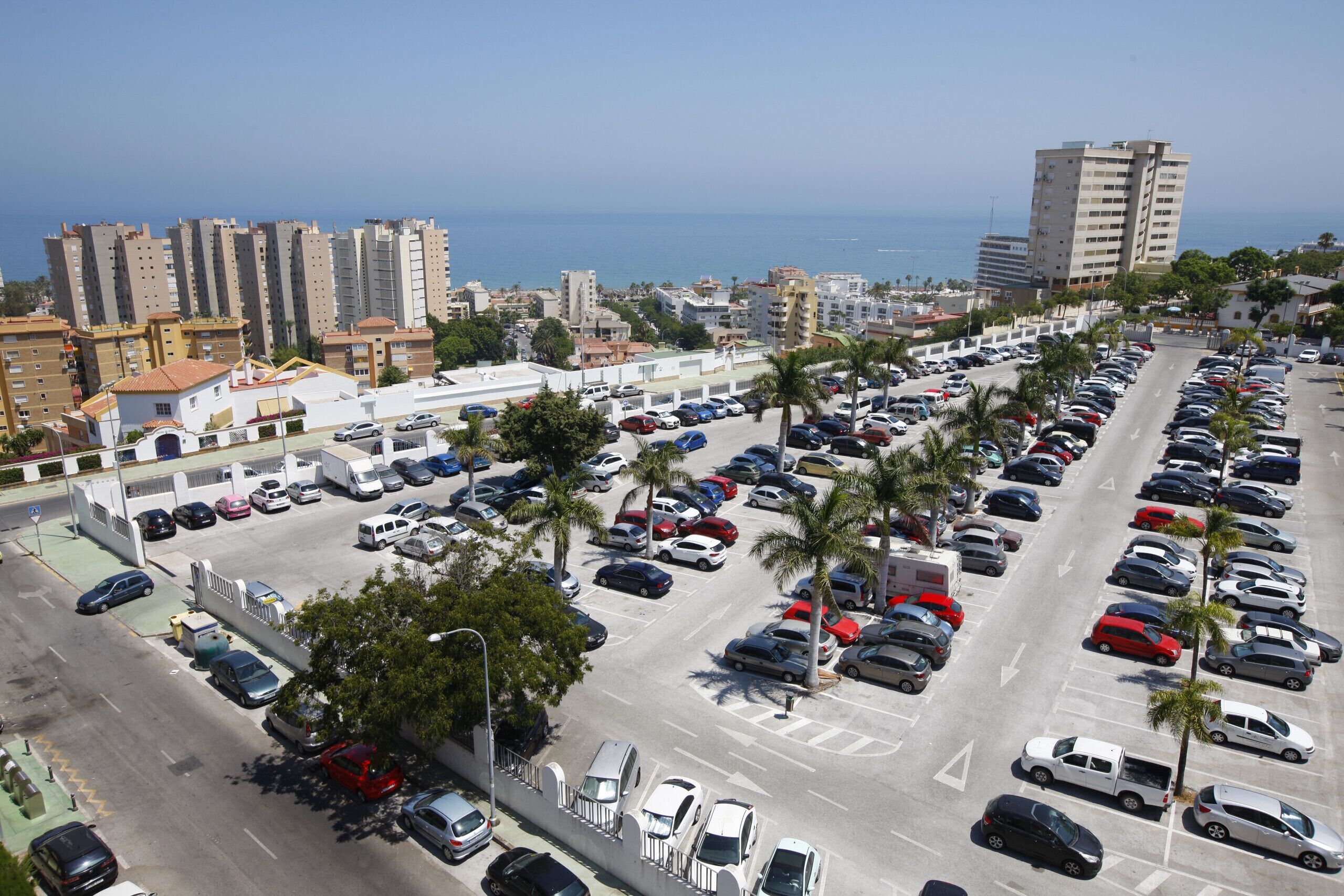 Un parcheggio con numerose file di auto parcheggiate, un edificio con tetto rosso e vista sul mare sullo sfondo.