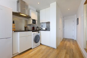 A compact kitchen with a washing machine, microwave, and wooden flooring. - Picasso Boutique (Torremolinos)