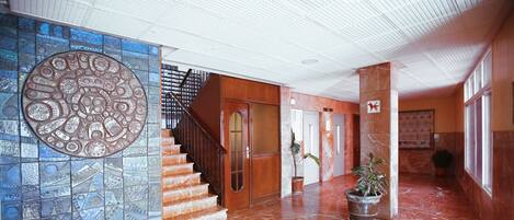 A lobby with a tiled wall, a staircase, and potted plants.