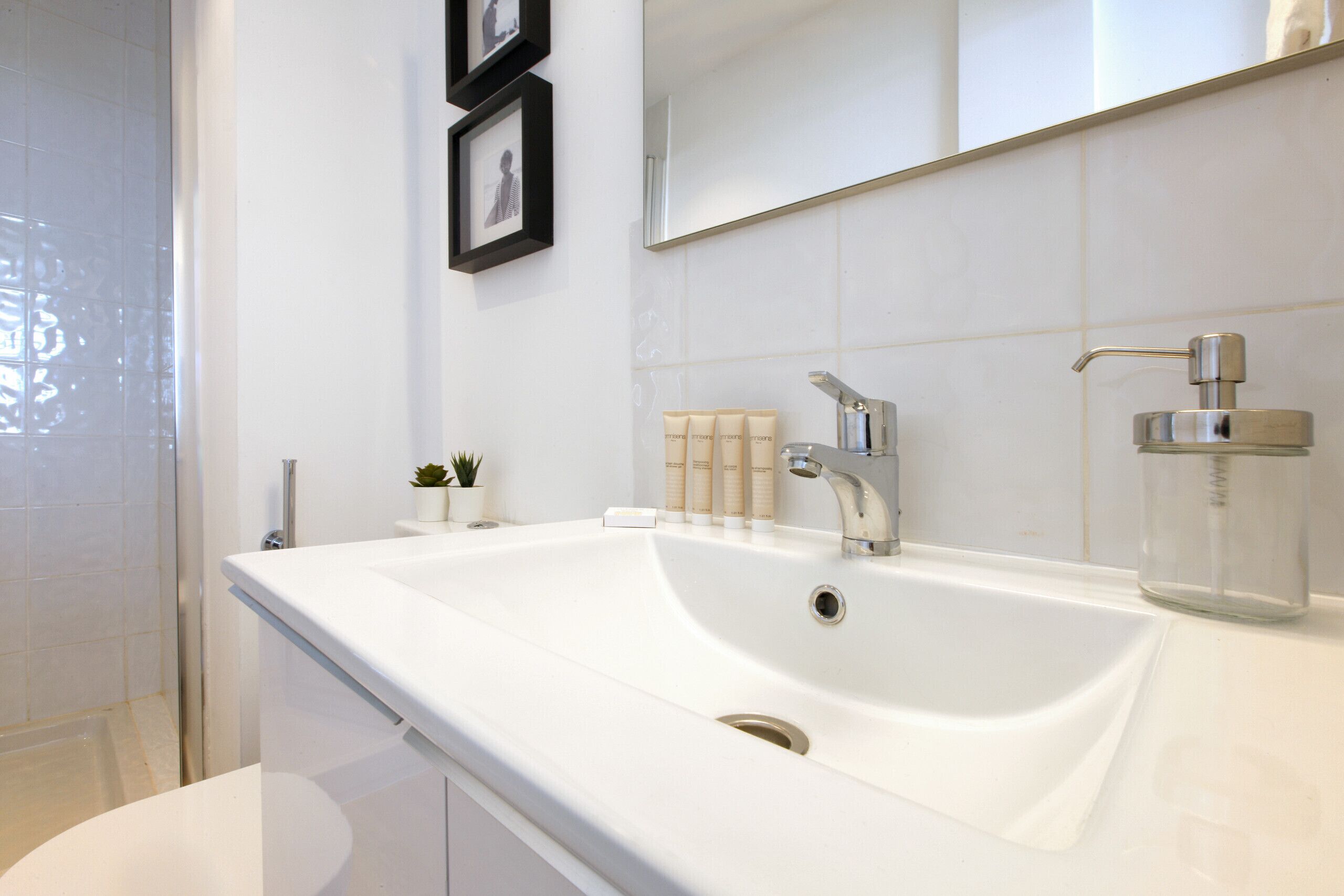 Une salle de bain moderne avec un lavabo blanc, un miroir et des photos encadrées accrochées au mur.