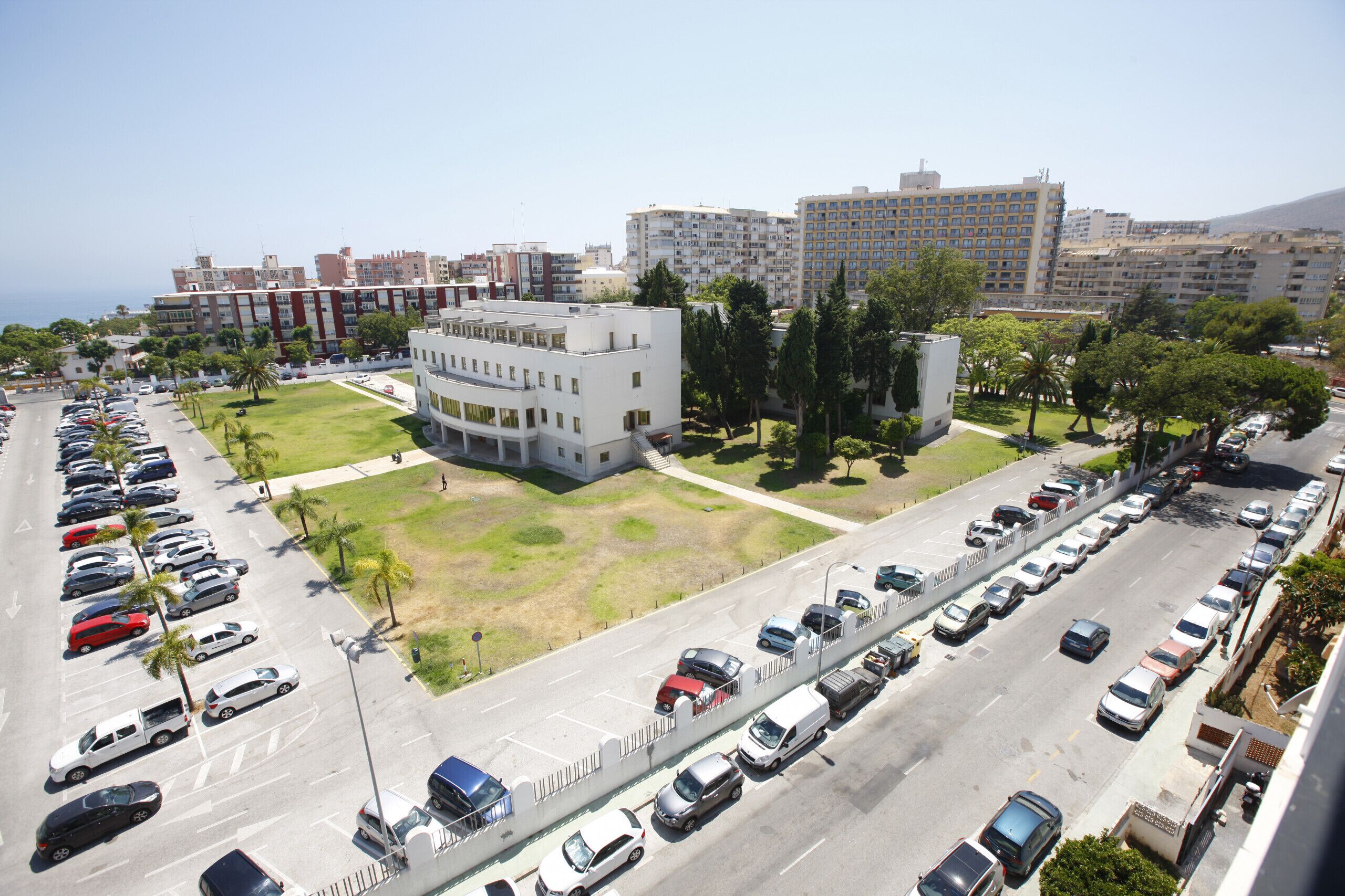 A multi-story hotel with a central courtyard, parking lot, and a view of the cityscape.