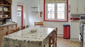 A kitchen with a dining table, chairs, a red trash bin, and a window with a view of buildings outside. - 3 bedroom accommodation in Scarborough (Scarborough)