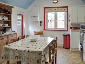 Una cocina con una mesa de comedor, sillas, un bote de basura rojo y una ventana con vista a edificios.