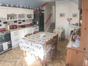 Una cocina con armarios blancos, un tostador rojo, una mesa de comedor de madera con mantel estampado y piso de parquete.