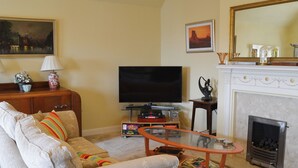 A living room with a sofa, television, fireplace, and a painting on the wall. - 3 bedroom accommodation in Scarborough (Scarborough)