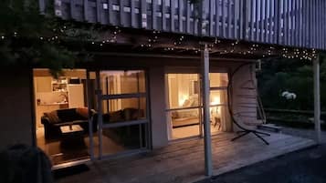 A modern house with a wooden deck, large windows, and a swing chair.