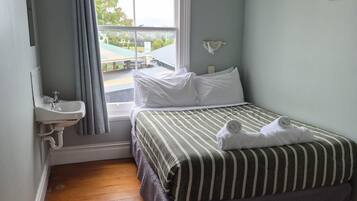 A bedroom with a bed, a window, a sink, and a painting on the wall.