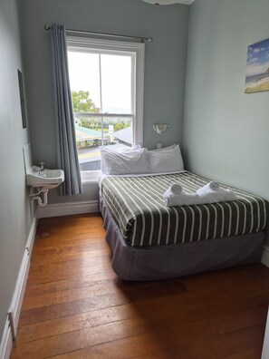 A bedroom with a bed, a window, a sink, and a painting on the wall. - Raglan Harbour View Hotel (Raglan)