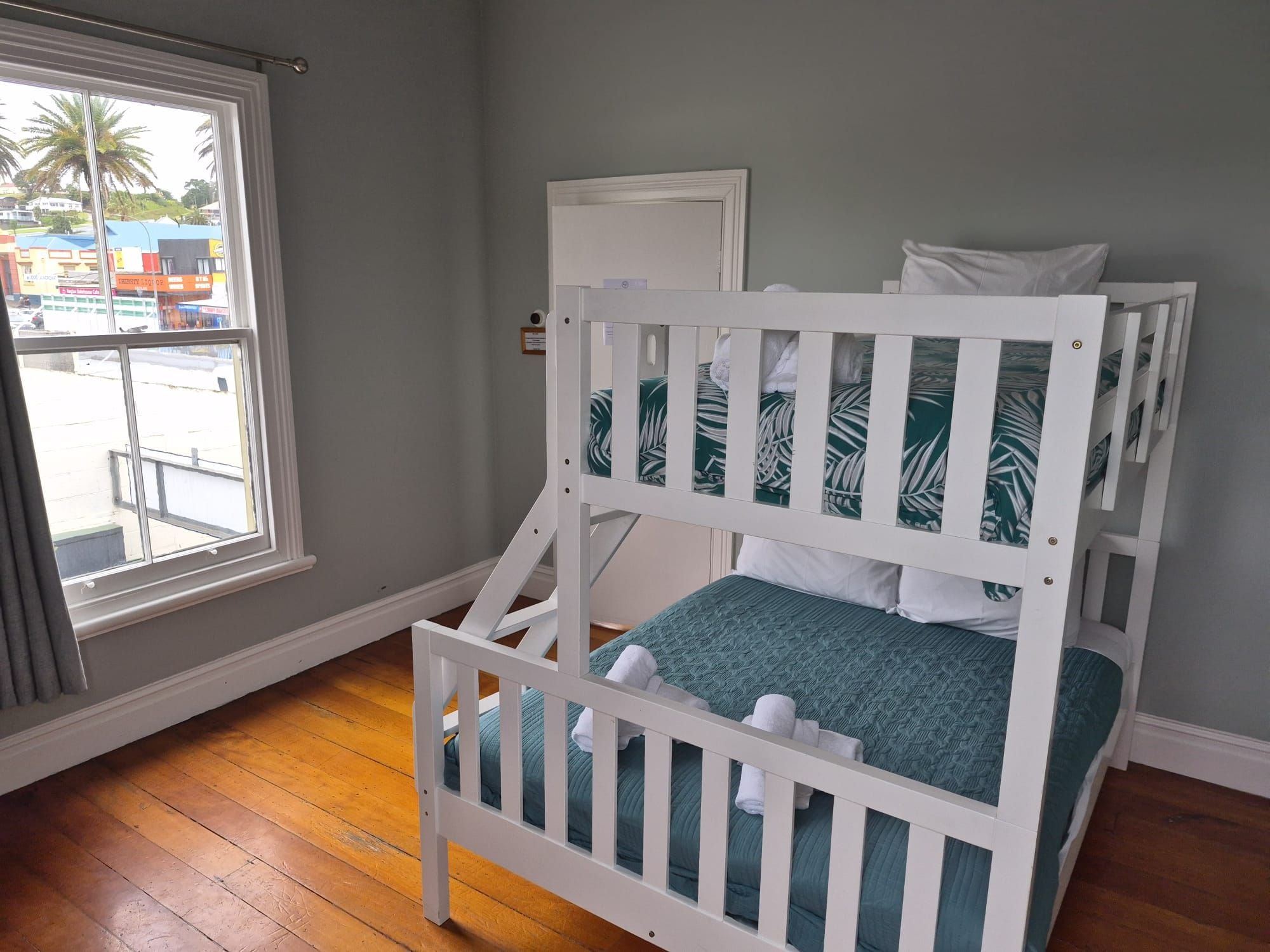 A bunk bed with a window view, a door, and a wooden floor.