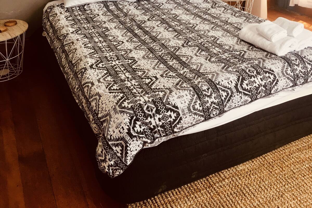 Habitación de hotel con cama, mesita de noche con lámpara, una pequeña mesa redonda con un cuenco y un cuadro colgado en la pared.