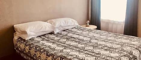 Un dormitorio con una cama, una mesita de noche, un cuadro en la pared y una ventana con cortinas.