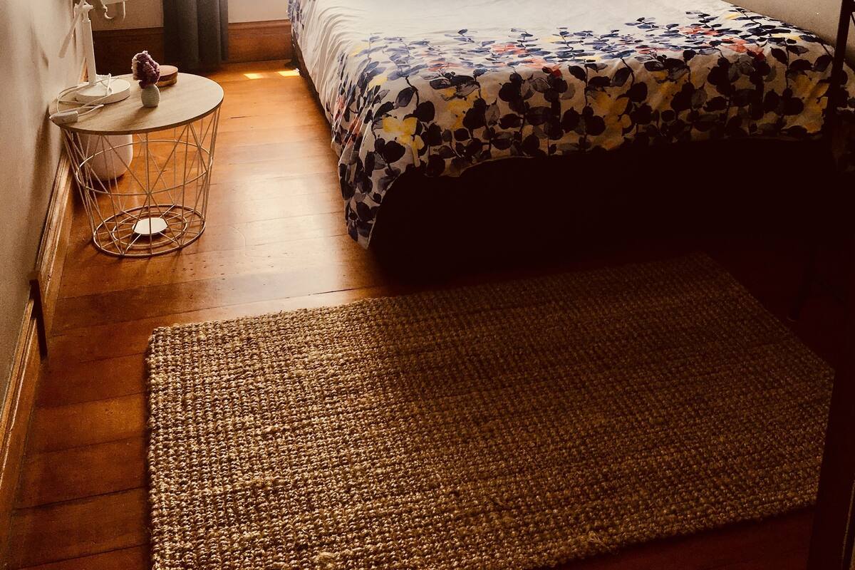 Un dormitorio con cama, mesita de noche con lámpara, ventana con cortinas, y una lámpara de pared.