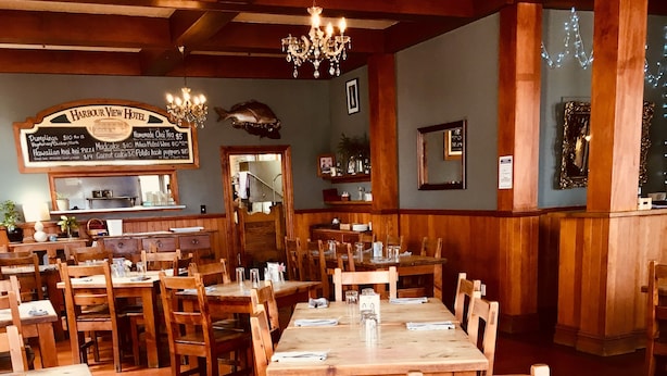 Un restaurante con mesas y sillas de madera, un tablero de menú y una araña.