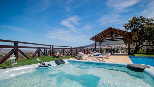 Una piscina con muelle de madera, sillones de descanso y una pérgola.