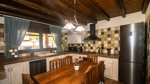 Una cocina con armarios de madera, un refrigerador de acero inoxidable, una mesa de comedor de madera con sillas y una lámpara colgante.