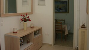 A room with a wooden console table, a vase with red flowers, a mirror, and a dining area with a table and chairs. - APARTMENT IN THE CENTER (Athens)