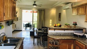 Cozinha com bancadas de granito, armários de madeira, espaço de refeições com cadeiras e vista para o exterior.