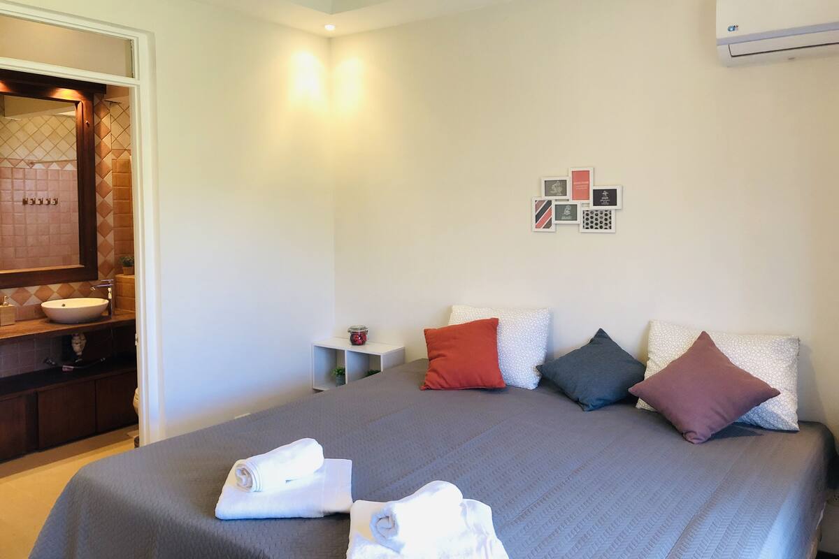 A hotel room with a bed, a bathroom with a sink, and a wall-mounted air conditioner.