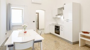 Cozinha moderna com armários brancos, forno embutido e janela com cortinas.