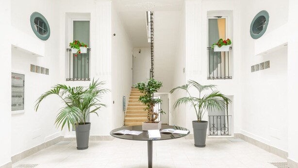 Um espaço interno amplo, com uma mesa redonda central, plantas em vasos e uma escada que leva a um andar superior.