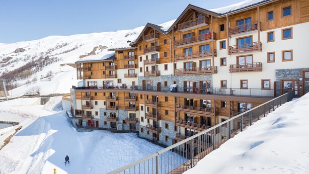 Un hotel de varios pisos con balcones de madera y pistas de esquí al fondo.