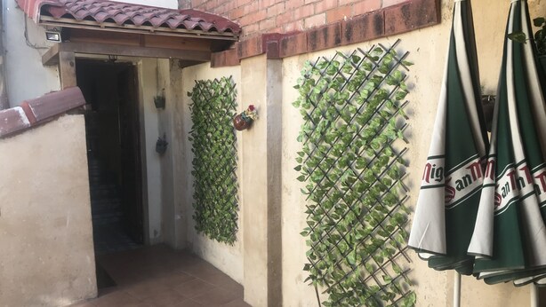 Une cour avec un sol carrelé, un mur en briques et un support à plantes en métal orné de feuillage verdoyant.