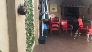 Une terrasse extérieure avec un four en briques, des chaises en plastique rouges et une chaise à l’effigie de Coca-Cola.