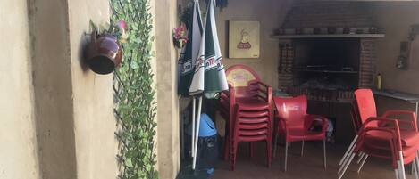 Un patio al aire libre con un horno de ladrillo, sillas de plástico rojo y una silla con la marca Coca-Cola.