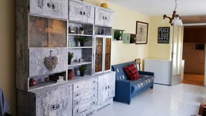 Un salon avec un grand meuble blanc doté de nombreuses étagères et de tiroirs, un canapé bleu avec un coussin rouge et un mur orné d’une affiche portant l’inscription « Paix, amour, bonheur ».