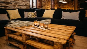 Une pièce rustique avec un banc en bois, un canapé noir orné de coussins à rayures et un mur en pierre.