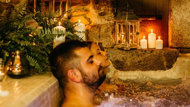 Une pièce aux murs de pierre, avec une baignoire, des bougies et une lanterne.