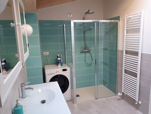 Ein modernes Badezimmer mit einer gläsernen Dusche, einer Waschmaschine und einem weißen Waschbecken.