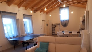 A living room with a ping pong table, a sofa with a cushion, and a dining area with chairs and a table. - LITTLE FROG on UNESCO Piedmont Langhe Monferrato WINE HILLS. Garden BBQ pingpong (agliano terme)