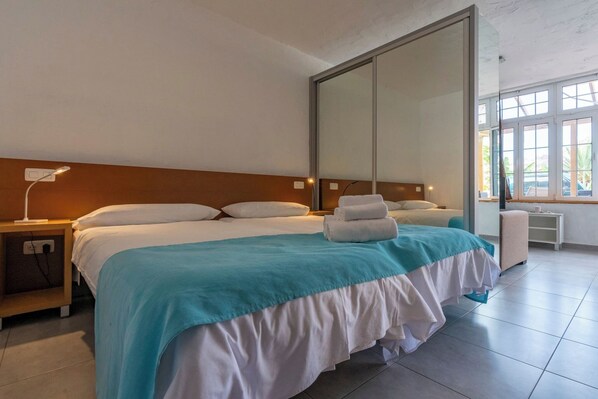 Hotellihuone, jossa on suuri sänky, yöpöytä lampun kanssa, työpöytä ja suuri peili.