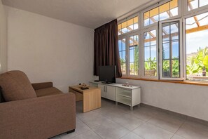A living room with a sofa, a TV on a white cabinet, and a window with curtains. - GC0282 Holiday house with shared pool in Mogán (Mogán)