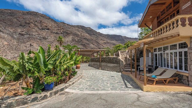 A stone-paved courtyard with a wooden pergola, potted plants, and a seating area with lounge chairs. - GC0282 Holiday house with shared pool in Mogán (Mogán)