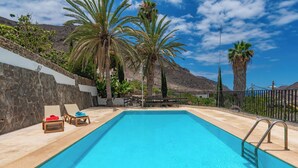 A swimming pool with lounge chairs and palm trees. - GC0282 Holiday house with shared pool in Mogán (Mogán)