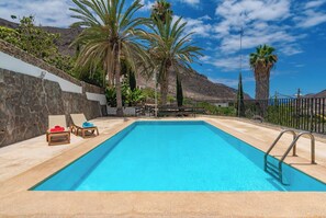 A rectangular pool with a clear blue water surface, surrounded by a stone wall and a metal fence.