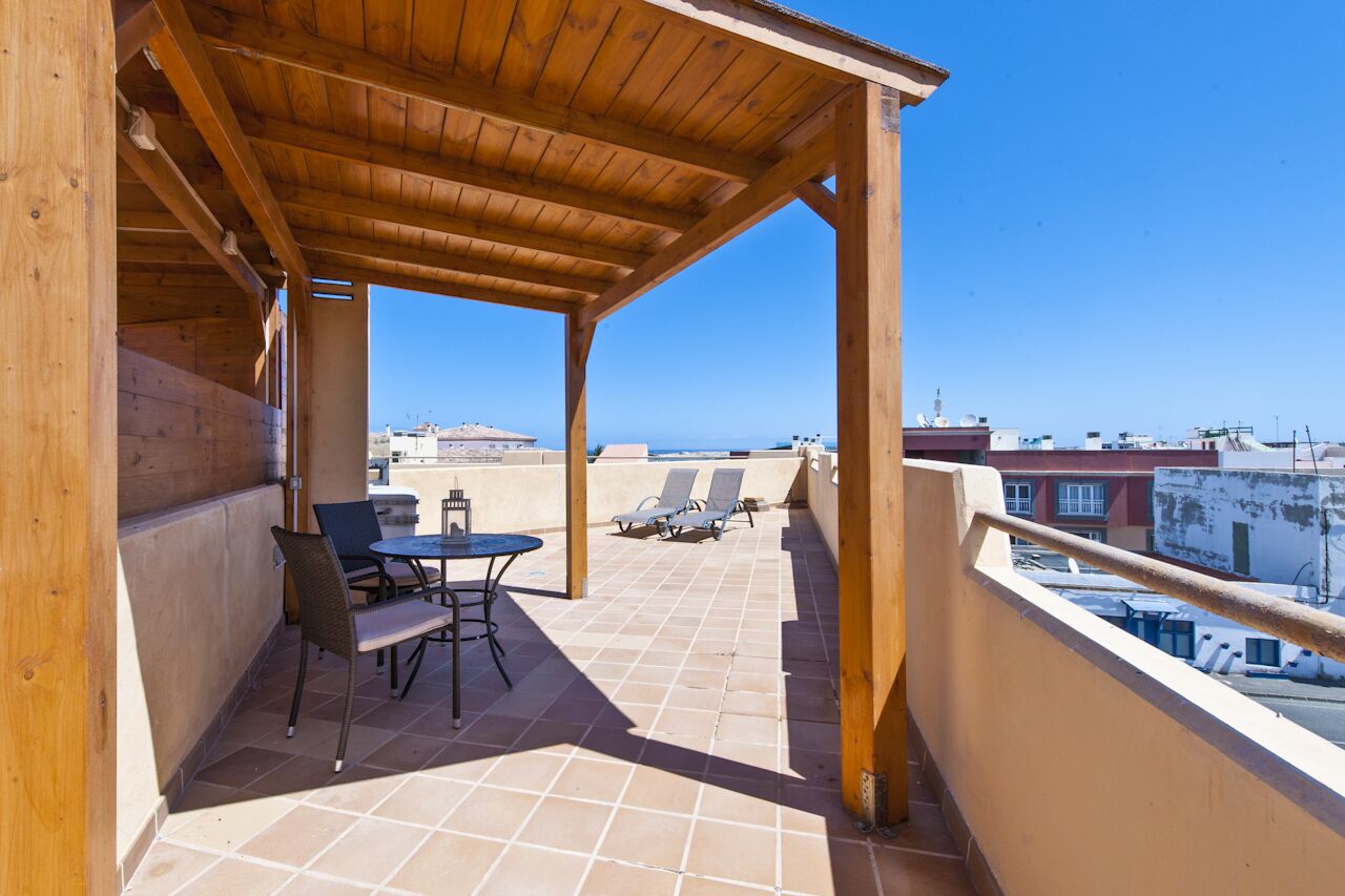 A covered outdoor area with a wooden pergola, a table with two chairs, and two sun loungers.