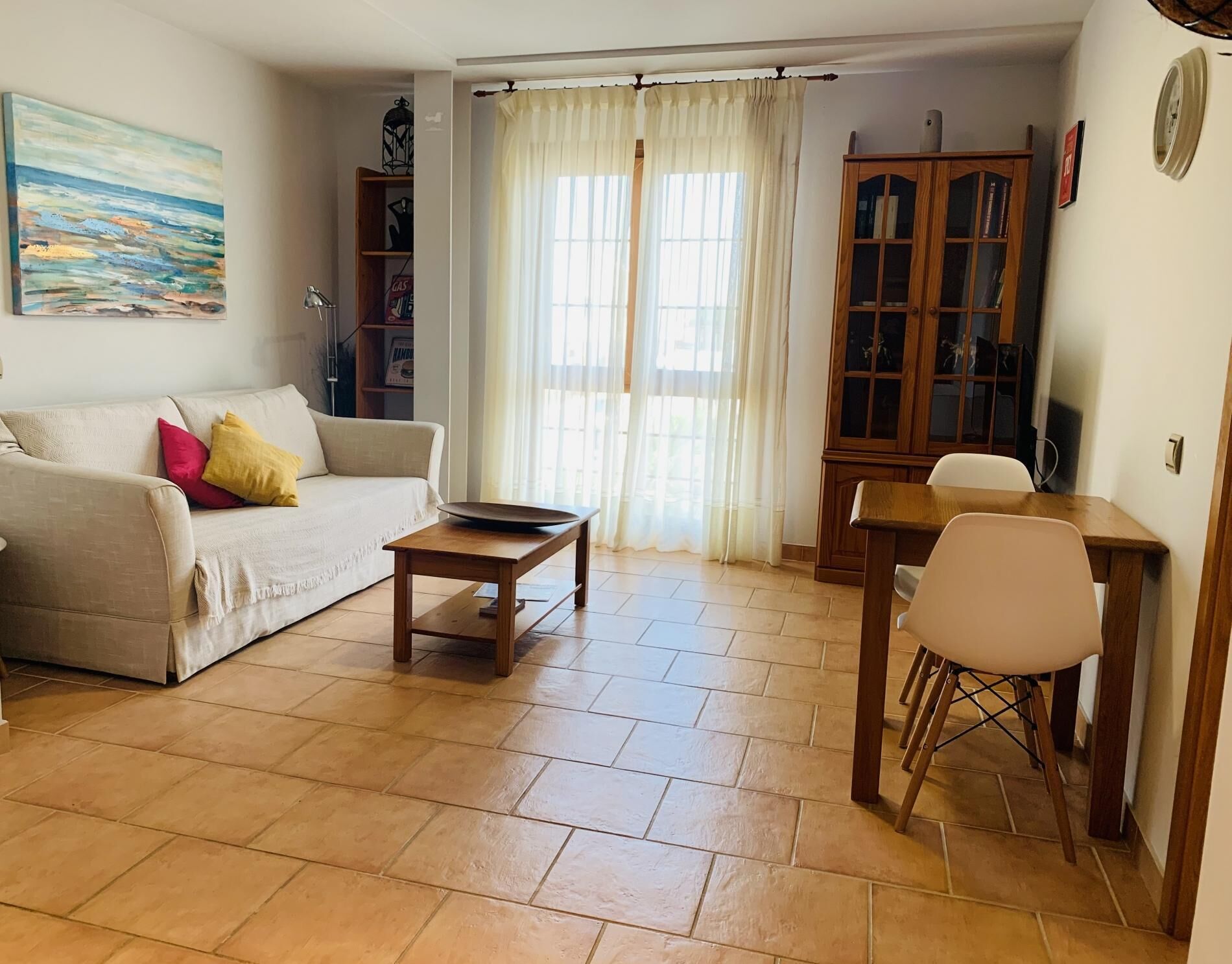 Un salon comprenant un canapé, une table basse, une table à manger avec des chaises, un meuble et un tableau accroché au mur.